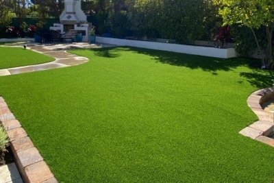 View of a vibrant green artificial lawn surrounded by landscaped areas, featuring a patio and outdoor seating, showcasing recent outdoor construction work.