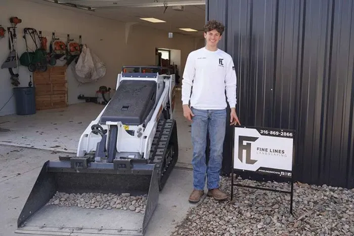 Man in white with mini bulldozer beside.