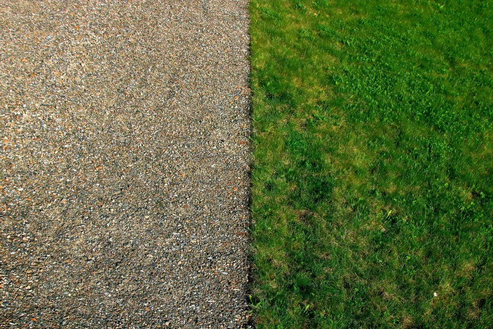 A clear divide between a gravel surface on the left and a lush green grass area on the right, showcasing the contrast between the two textures.